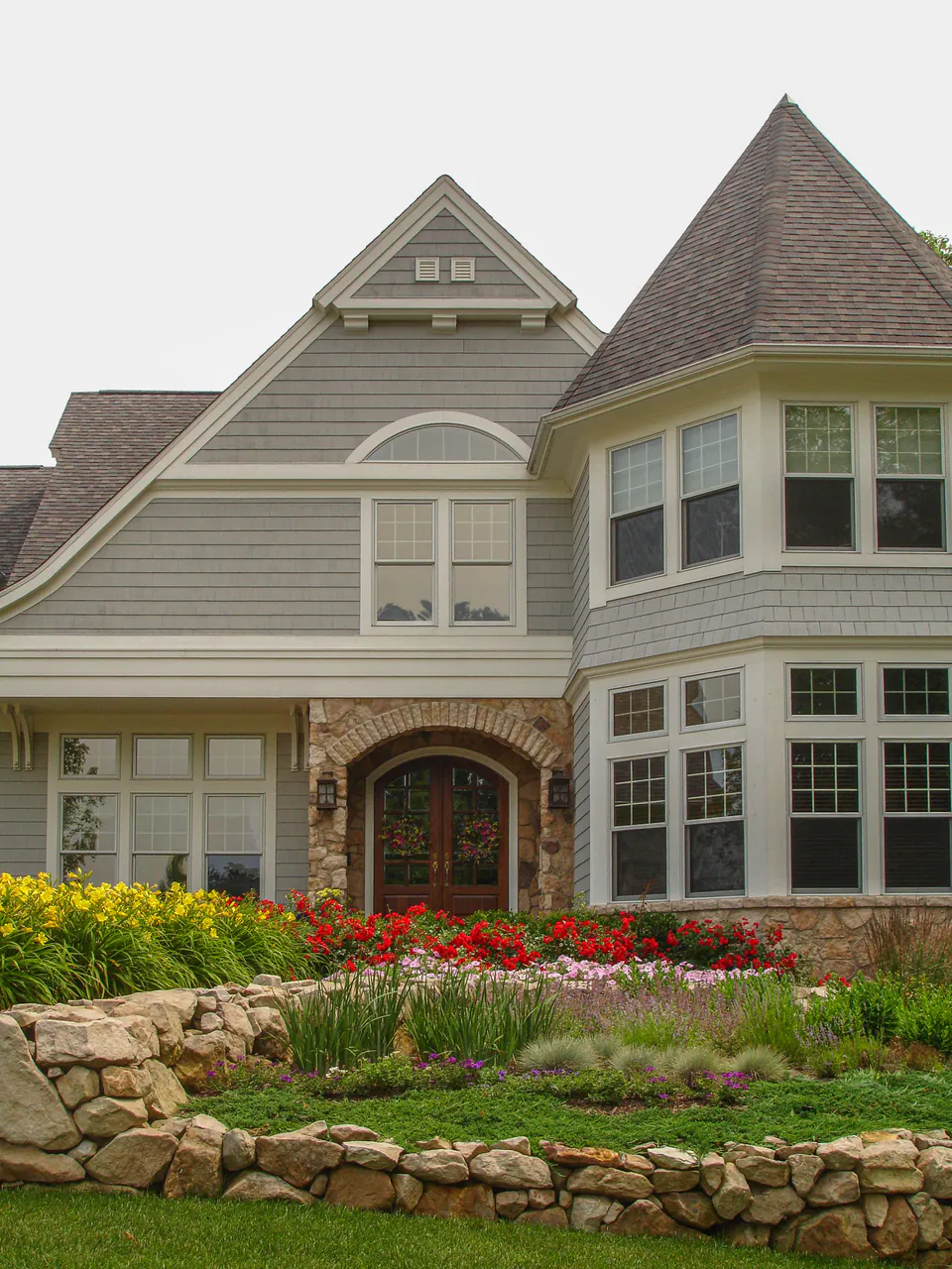Estate home entry with stone garden wall, yellow flowers, red seasonal color, shrubs, and lawn